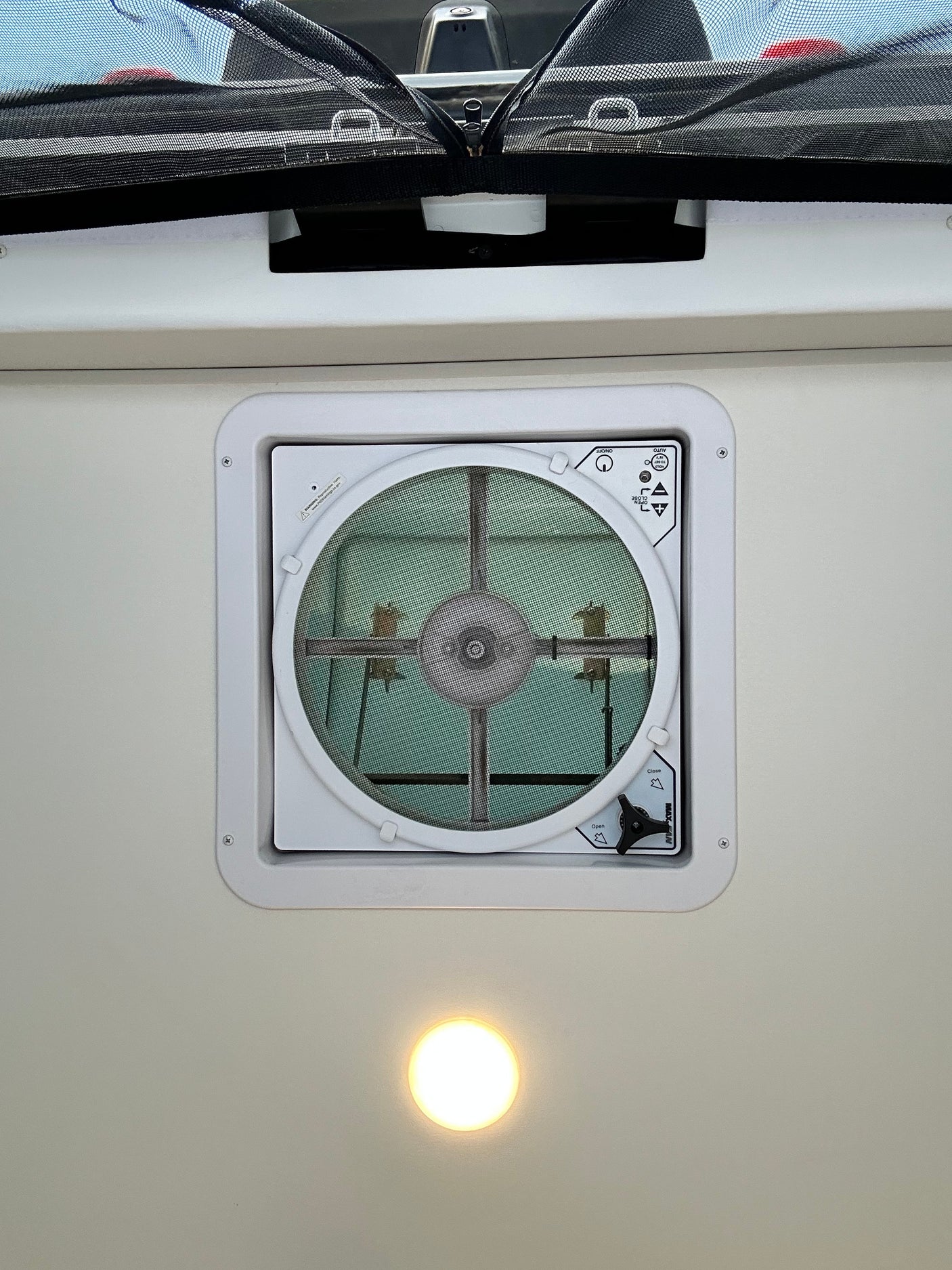 RV rental overhead view: MaxxAir ceiling vent fan with screen, an overhead light, and a black mesh privacy screen.