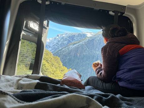 Cozy RV rental experience: Person enjoying a snack with stunning snow-capped mountain views from the comfortable interior.