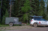 Adventure-ready: an RV rental trailer and SUV with raft, parked by a dense forest. Ideal for exploring nature.