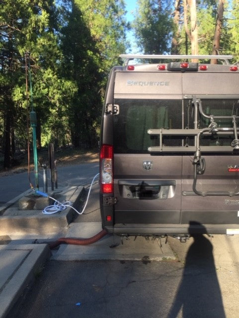 RV rental: A grey 'Sequence' camper van at a sunny campsite, hooked up to water & sewer. A bike rack is on its rear.