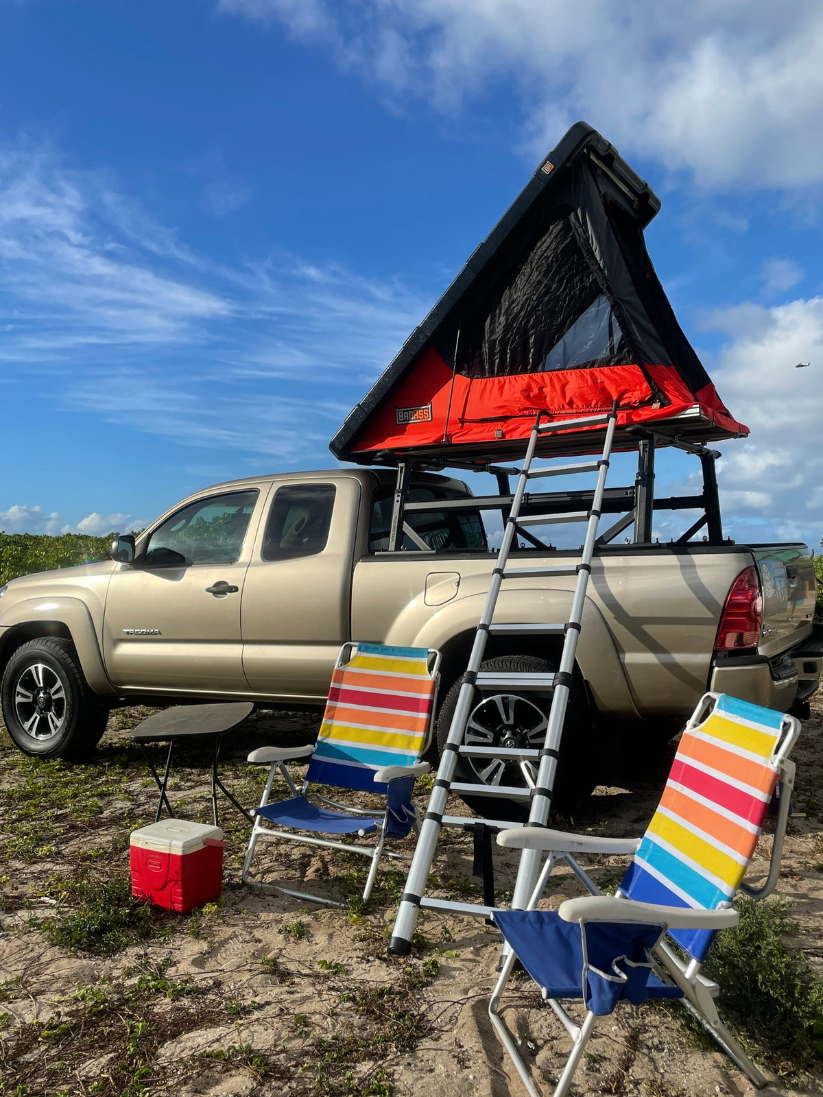 Outdoor adventure awaits! A tan pickup with a rooftop tent, ladder, beach chairs, and cooler on sandy ground. Explore our RV rental options. — photo 13