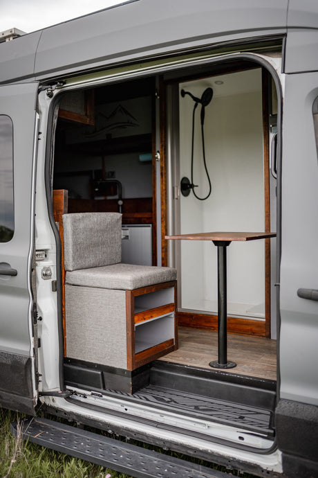 RV rental van interior: cozy seat, dining table, and compact shower for mobile living.