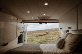 Comfortable rv rental interior: bed, cabinets, and open doors revealing a vast green, hilly landscape. Perfect camper van escape.