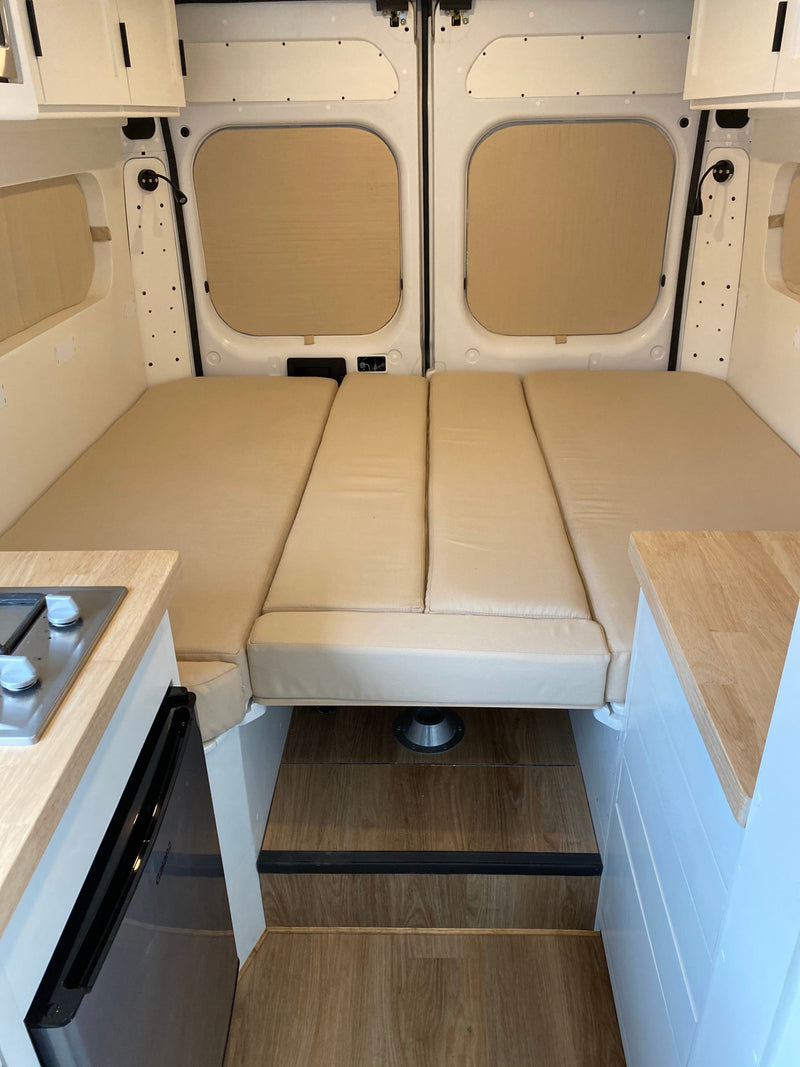 Compact RV rental interior featuring a convertible bed, kitchenette with stove & fridge, and wood accents. — photo 13