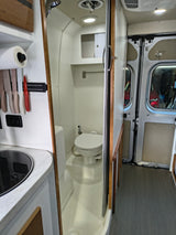 This rv rental shows a compact interior: a narrow wet bath with a toilet on the right, and a kitchen sink to the left.
