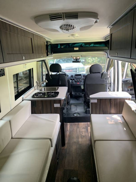 Inside an RV rental: a spacious camper van interior with kitchen, living/sleeping areas, and front cab view, ideal for travel.