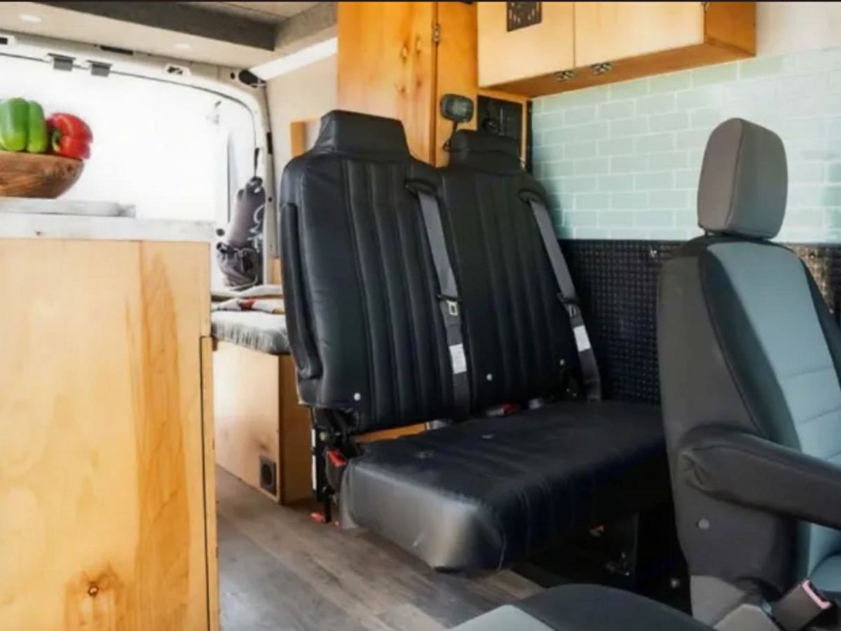  parked by the ocean. Open doors reveal a cozy wooden interior.|Inside this RV rental: versatile seating — photo 2