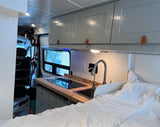 Inside an rv rental: functional kitchenette with cooktop & sink, comfy bed, and ample overhead cabinets.
