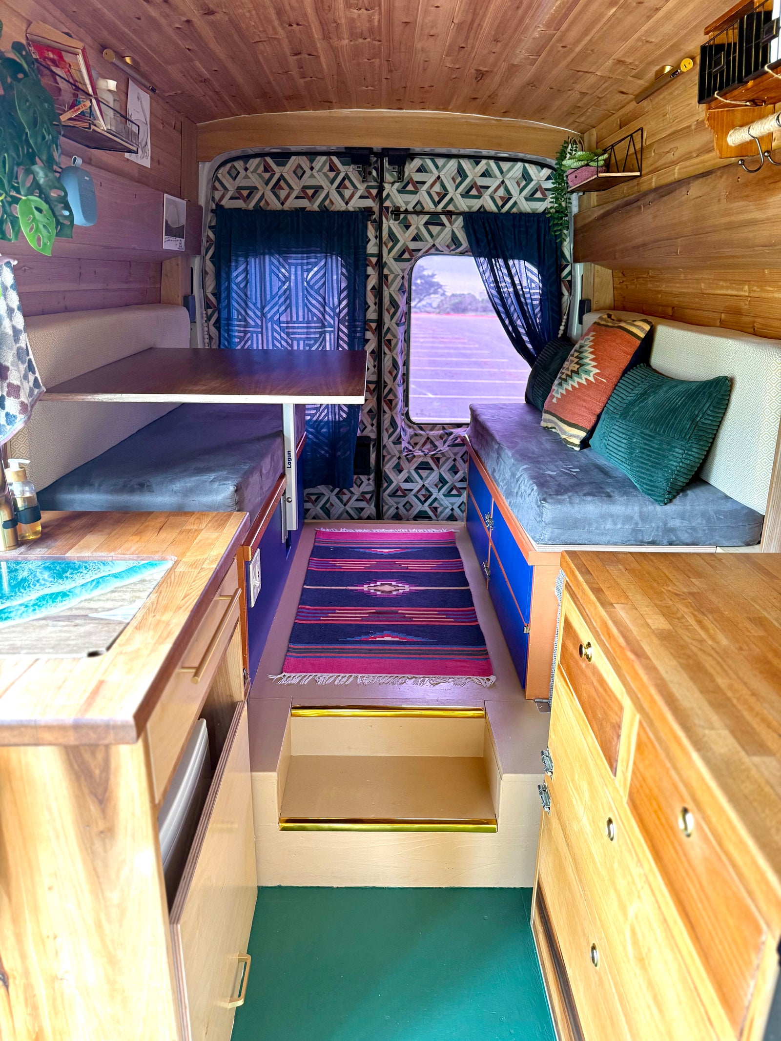 Inside a stylish RV rental: wooden interior, kitchenette with unique sink, dining area, cozy seating, and vibrant rug.