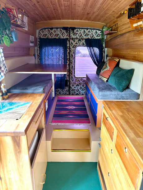 Inside a stylish RV rental: wooden interior, kitchenette with unique sink, dining area, cozy seating, and vibrant rug.