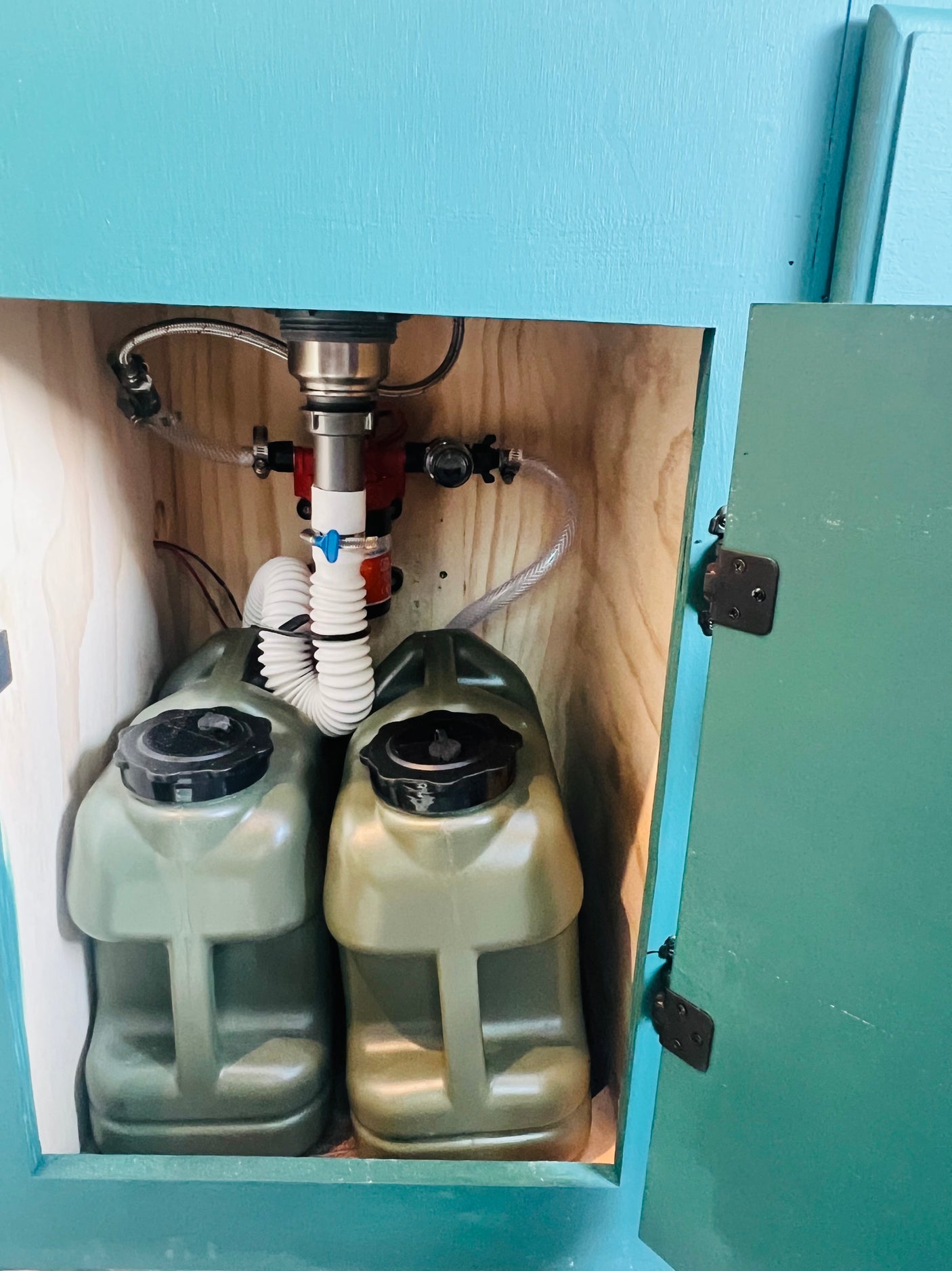 RV rental under-sink water system with two portable green tanks, hoses, and plumbing for compact, self-contained use.