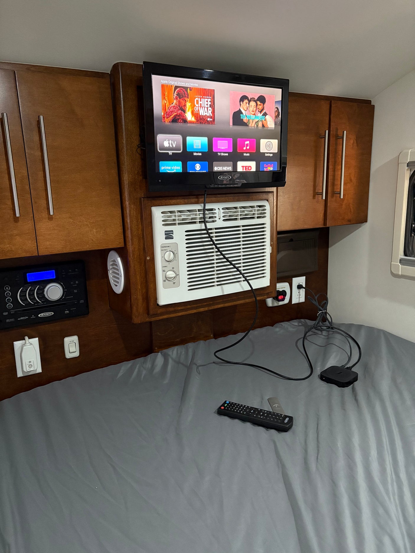 Cozy rv rental bedroom equipped with a mounted TV (Apple TV), AC, & Jensen stereo for ultimate comfort on the road.
