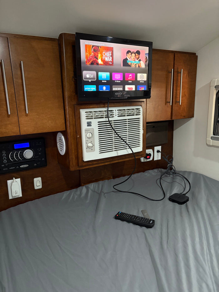 Cozy rv rental bedroom equipped with a mounted TV (Apple TV), AC, & Jensen stereo for ultimate comfort on the road.