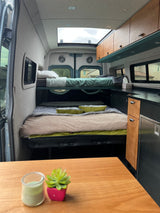 RV rental interior view: bunk beds, lower bed, compact kitchen with fridge/cabinets, and bright skylight above.