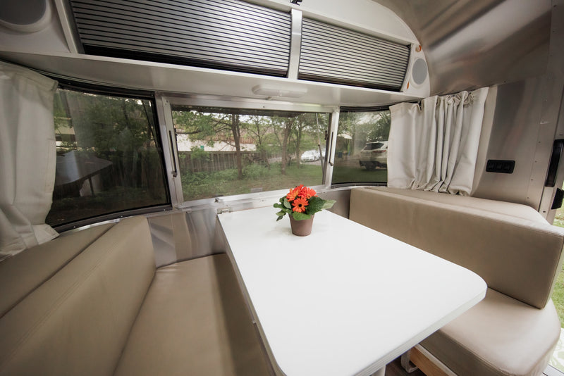 Inside this RV rental: a bright dinette with panoramic windows, comfy beige cushions, and a white table with flowers. Enjoy the scenic views! — photo 14