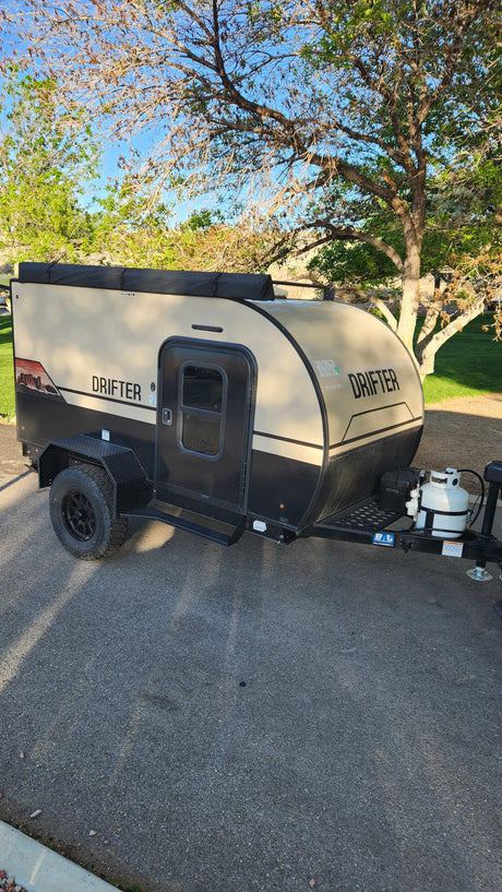 Compact, tan & black 'DRIFTER' teardrop camper, perfect for your next RV rental adventure, parked on asphalt.