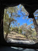 View from inside an RV rental tent, revealing a sunny forest and clear blue sky. Ideal for outdoor camping and adventure.