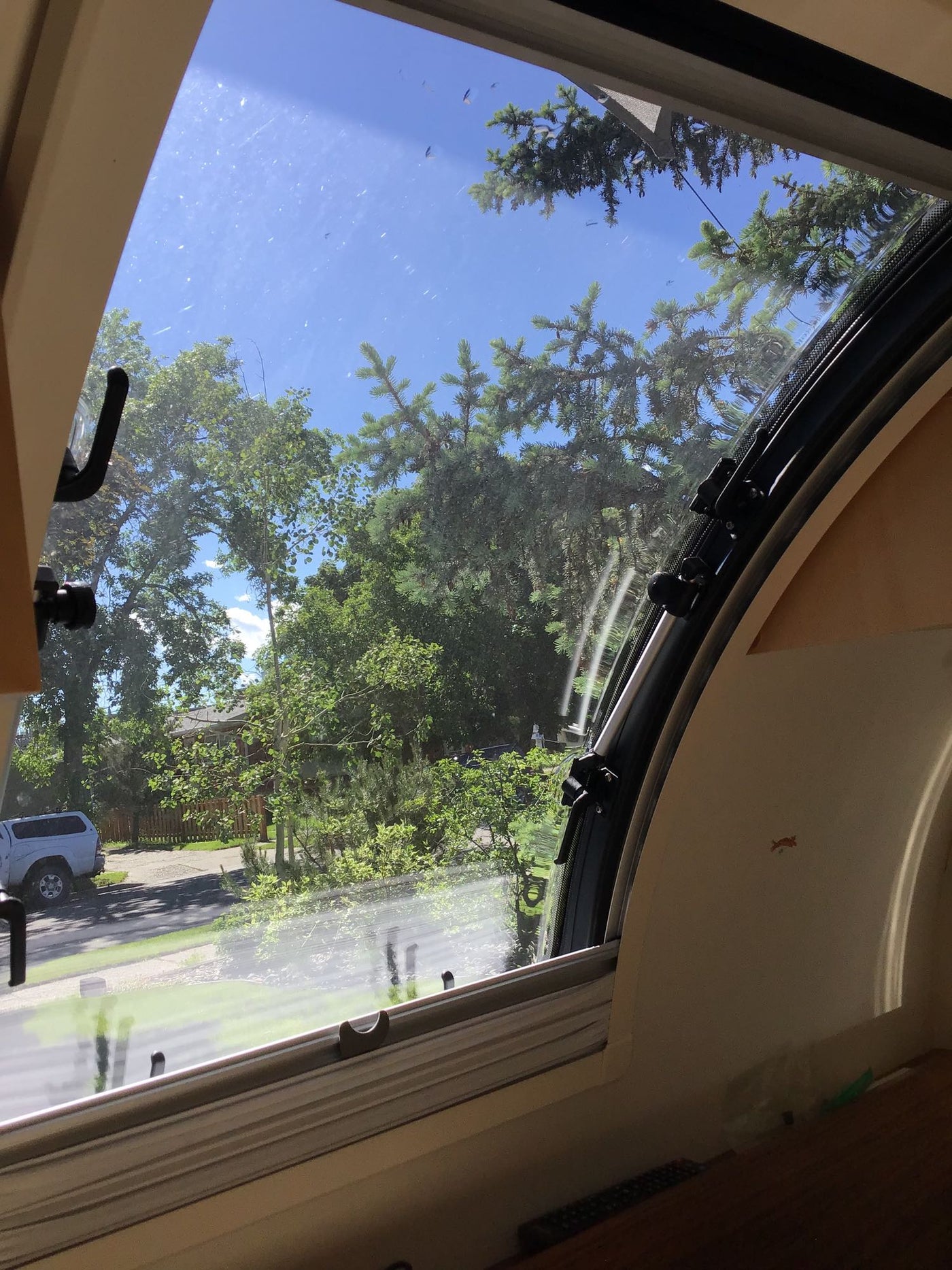 Curved window view from an rv rental showing a sunny sky, green trees, and a white truck parked outside. — photo 12