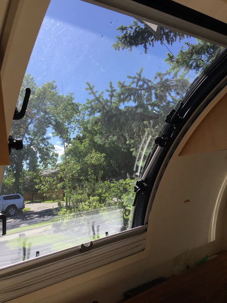 Curved window view from an rv rental showing a sunny sky, green trees, and a white truck parked outside.