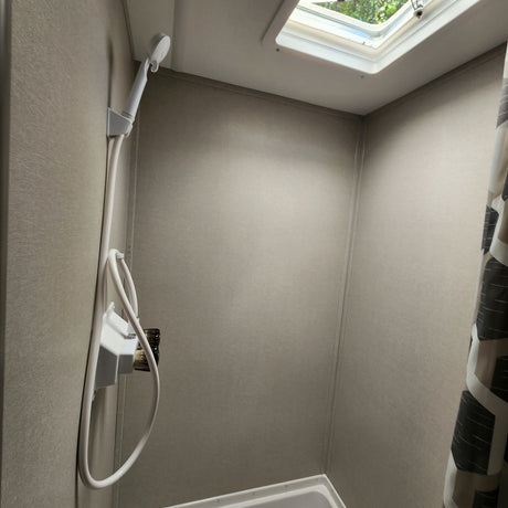 Inside an RV rental shower: a compact space with a handheld shower, neutral walls, and a skylight for natural light.