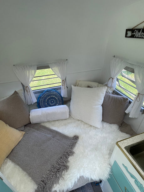 Cozy RV rental interior features a bed piled with white, grey, and blue mandala pillows, a soft fur rug, and grey blanket.