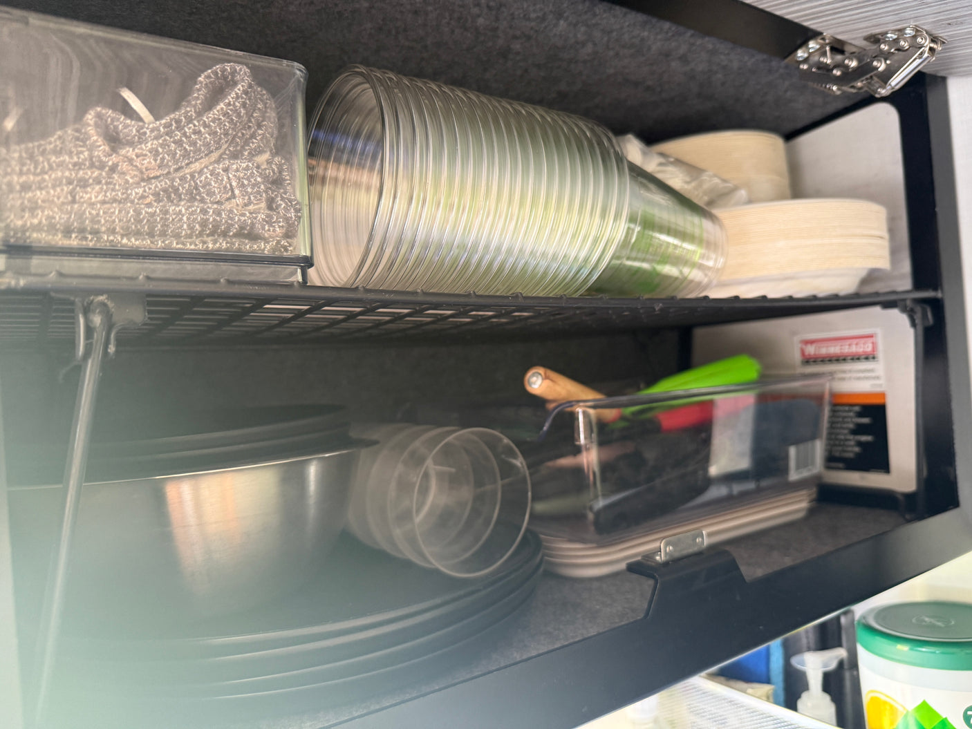 Compact, well-organized RV rental kitchen cabinet with plates, cups, and cooking tools.