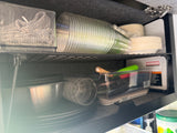 Compact, well-organized RV rental kitchen cabinet with plates, cups, and cooking tools.