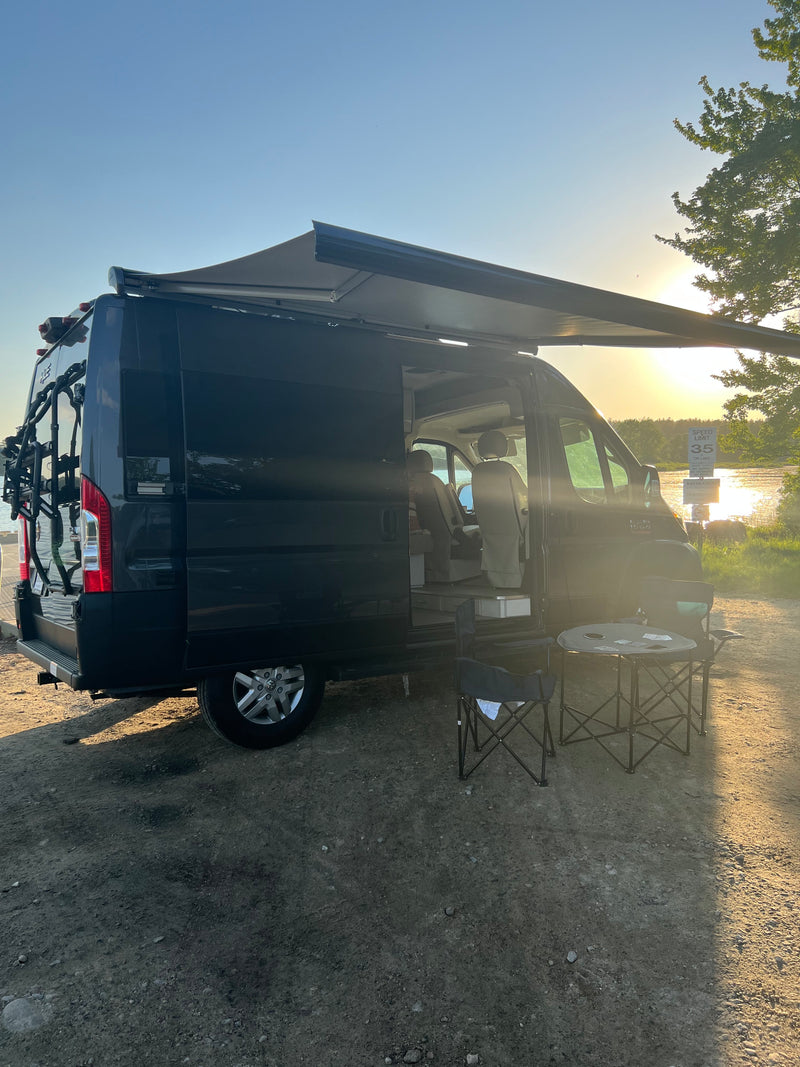 RV rental camper van with extended awning, chairs, and table set up by a sunlit lake, ready for outdoor living. — photo 7