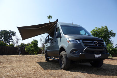 Grey Mercedes Sprinter camper van with extended awning, parked outdoors. Ready for your RV rental adventure.