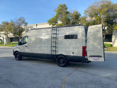 Light grey Sprinter camper van, perfect for RV rental, with a side ladder & open rear doors.