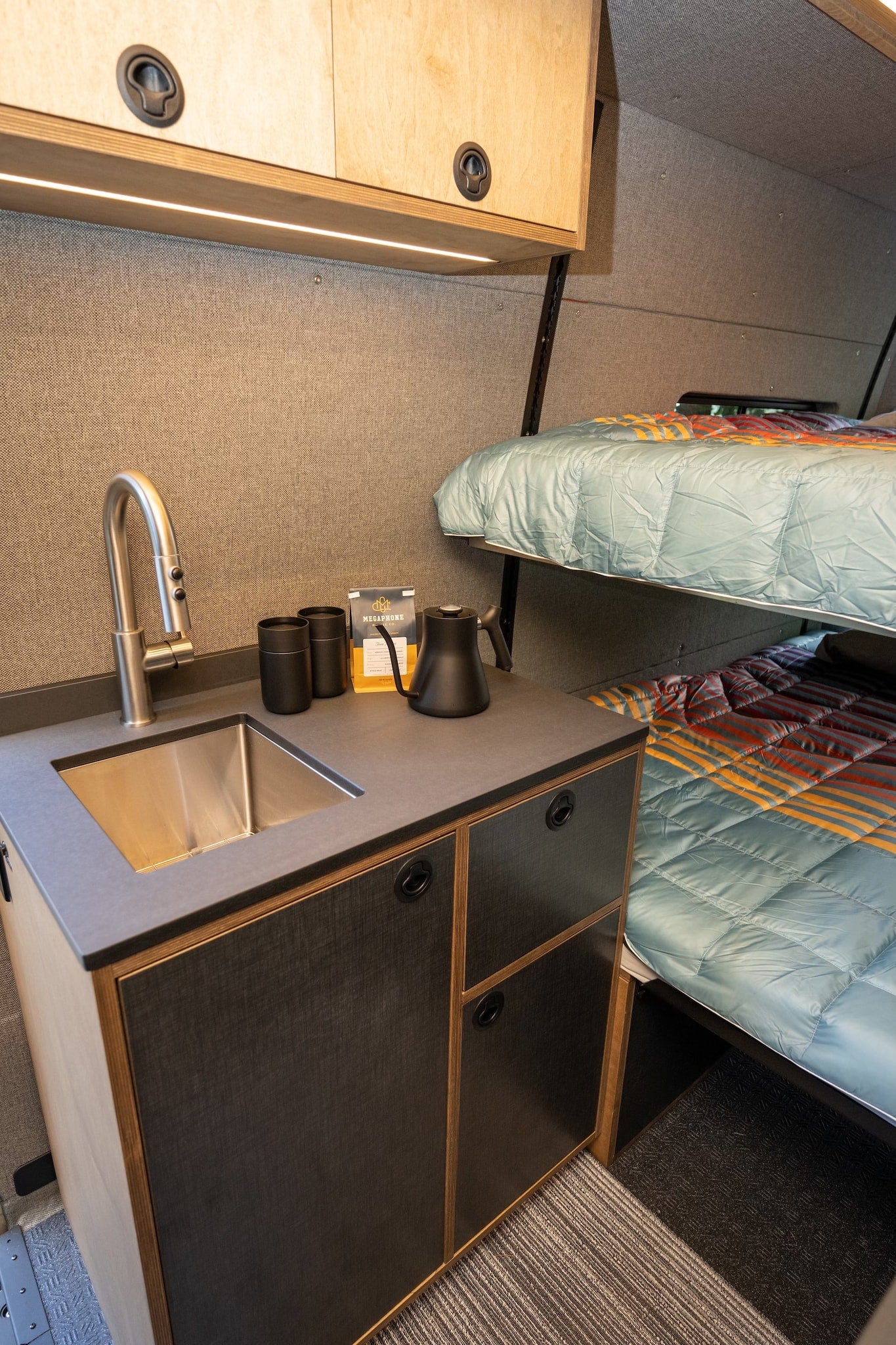 rv rental interior showcasing a compact kitchenette with sink & coffee station, plus stacked bunk beds with vibrant quilts. — photo 10