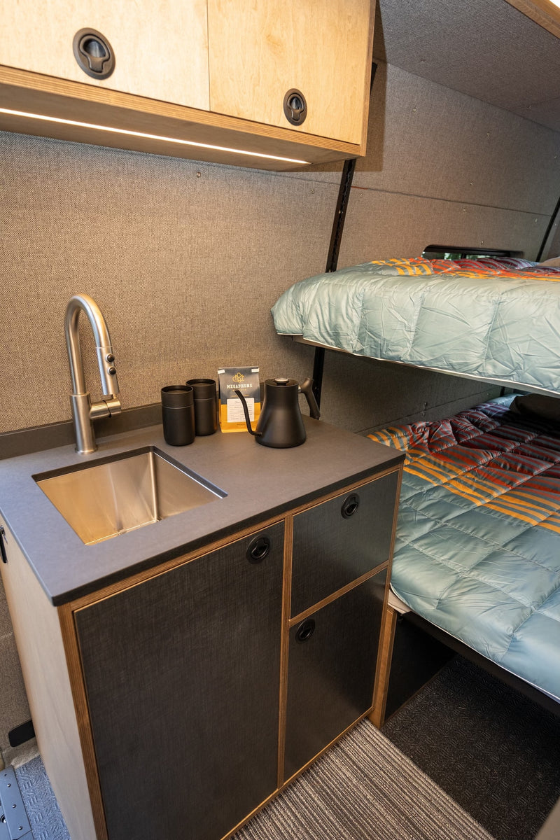 rv rental interior showcasing a compact kitchenette with sink & coffee station, plus stacked bunk beds with vibrant quilts. — photo 10