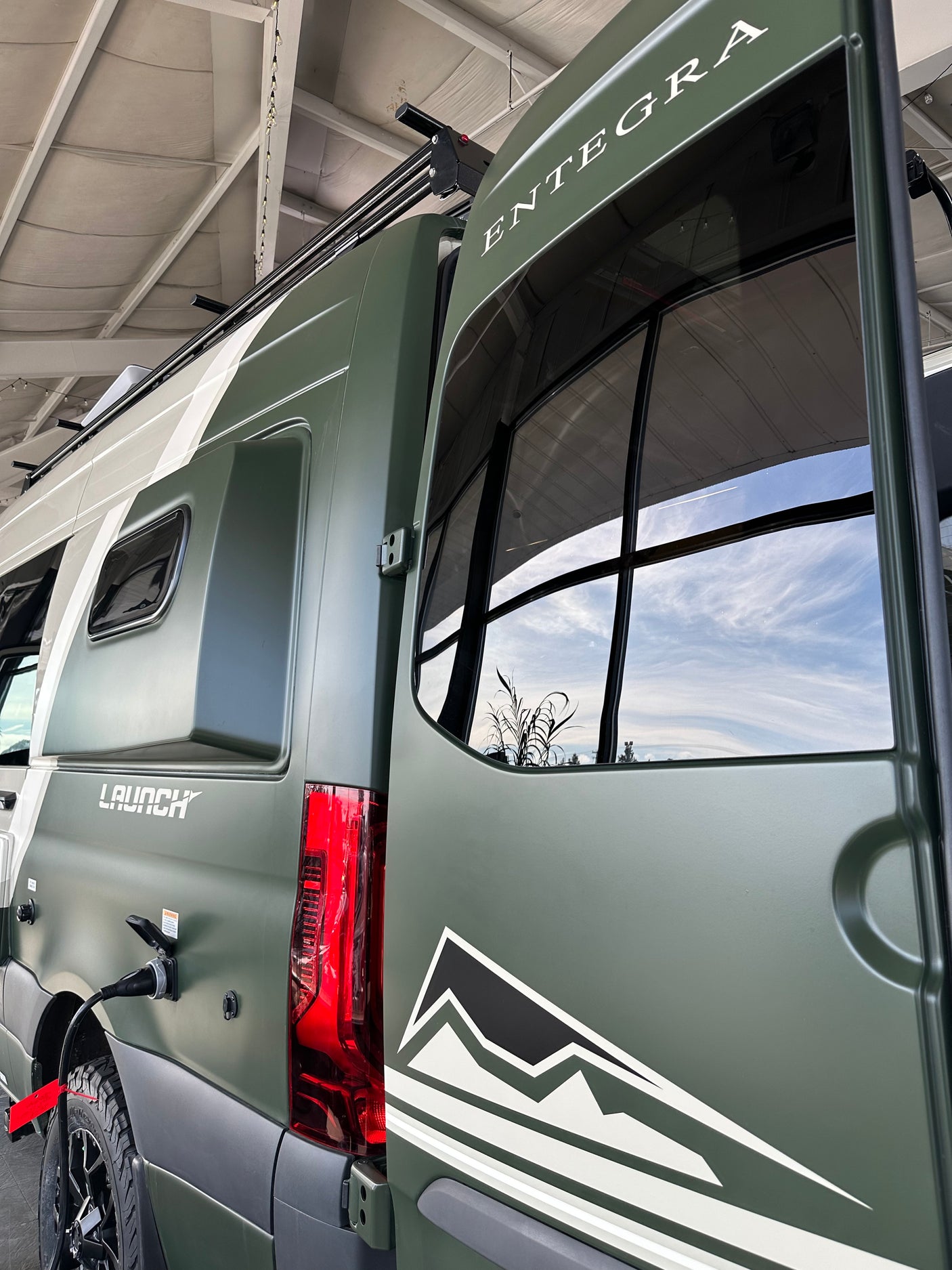 Matte green Entegra Launch RV, perfect for rv rental adventures, featuring open rear door and power hookup.