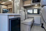 Inside an RV rental: kitchen counter, fridge, passenger seats, microwave, and a shower area, with a desert view.