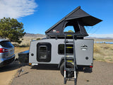 RV rental setup: Grey Escapade camper trailer with NaturNest rooftop tent & ladder, hitched to a Subaru. Ready for outdoor adventure.