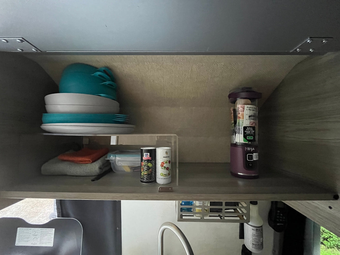 Organized RV rental kitchen cabinet with stacked dishes, spices, and a Ninja blender. Practical setup for compact spaces. — photo 11