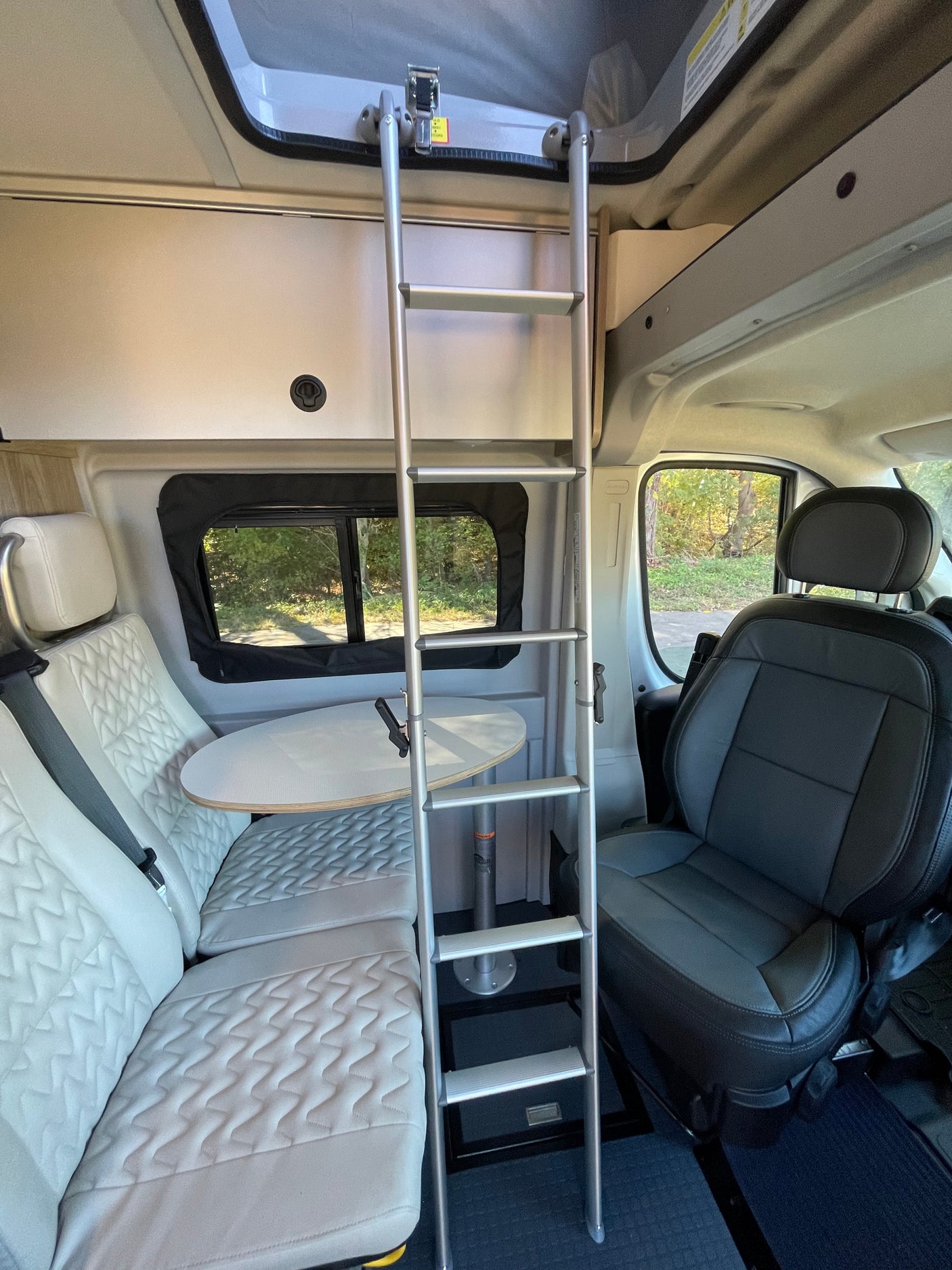 RV rental interior view: ladder to an overhead bed, dinette with light upholstery, and a dark gray driver's seat.