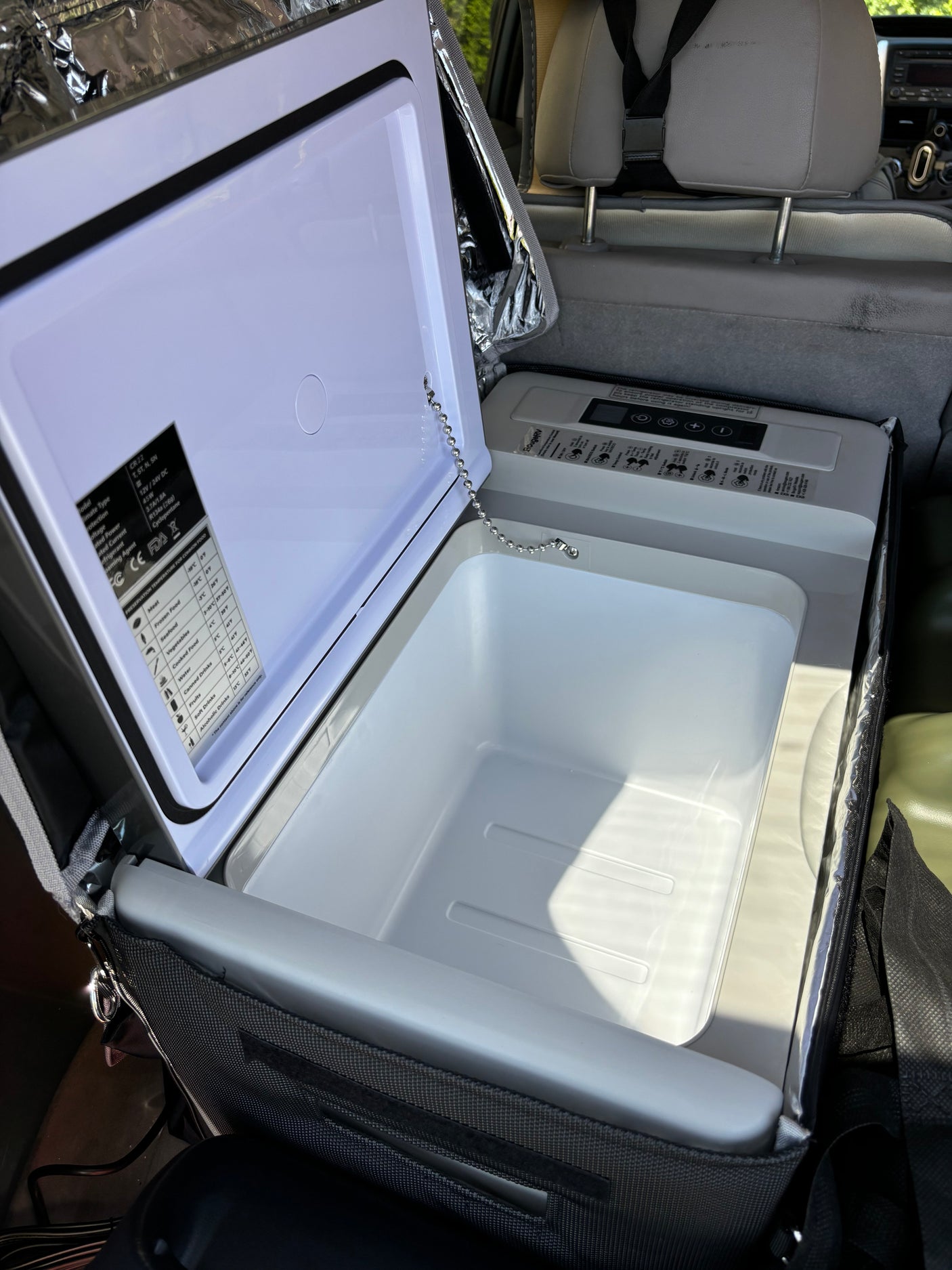 Inside an RV rental, an open portable electric cooler with its empty interior & control panel awaits travel.