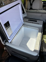 Inside an RV rental, an open portable electric cooler with its empty interior & control panel awaits travel.