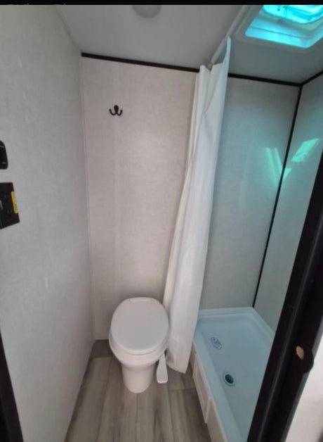 Inside an RV rental, this compact bathroom features a toilet, shower, and ceiling skylight, ideal for travelers.