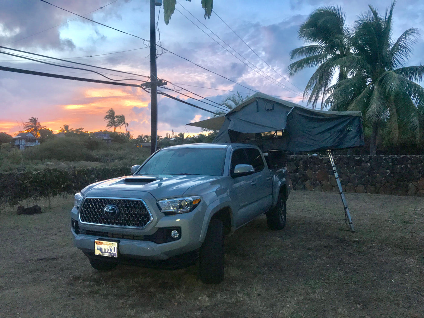 A grey Toyota Tacoma with a deployed rooftop tent, perfect for an RV rental adventure under a vibrant sunset sky.