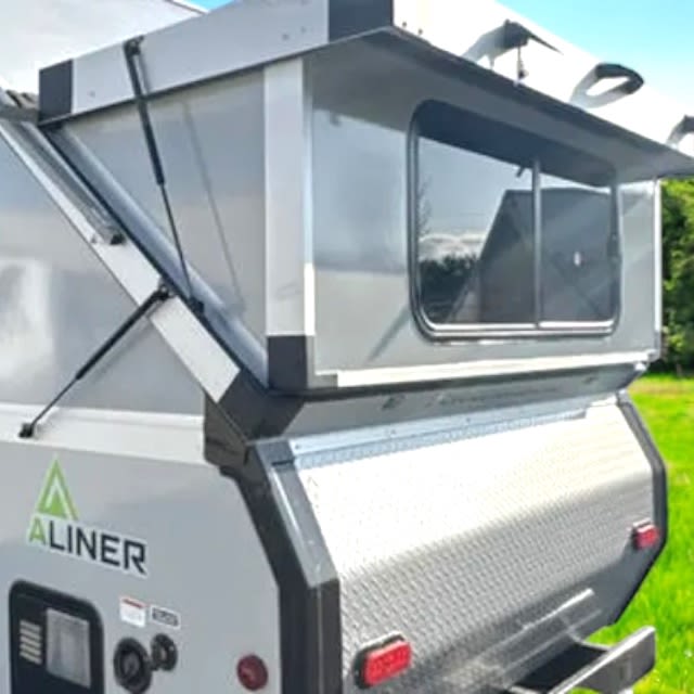 Rear view of a grey A-Liner pop-up RV rental, with its roof raised by struts, revealing a clear window.