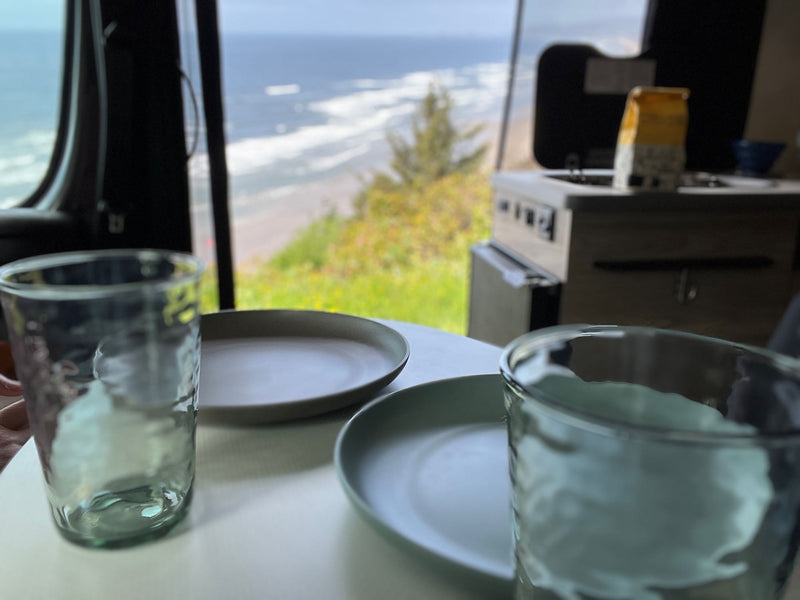  perfect for your travels.|Cozy RV rental dining setup with plates & glasses by a large window overlooking a stunning ocean beach.|Inside a functional RV rental: discover the compact kitchen — photo 6