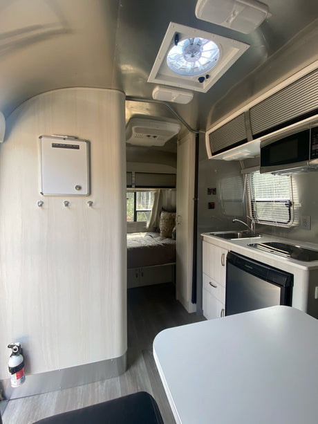 Step inside this modern RV rental, featuring a compact kitchen, dining area, and cozy bedroom ready for your travels.