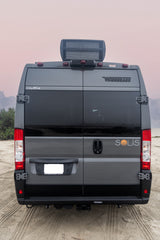 Rear view of a gray Winnebago Solis rv rental van on a sandy beach, with its distinct "Solis" sunset logo.