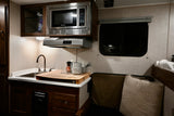 Compact RV rental kitchen features microwave, sink, and adjacent seating area with window, ideal for road trips.