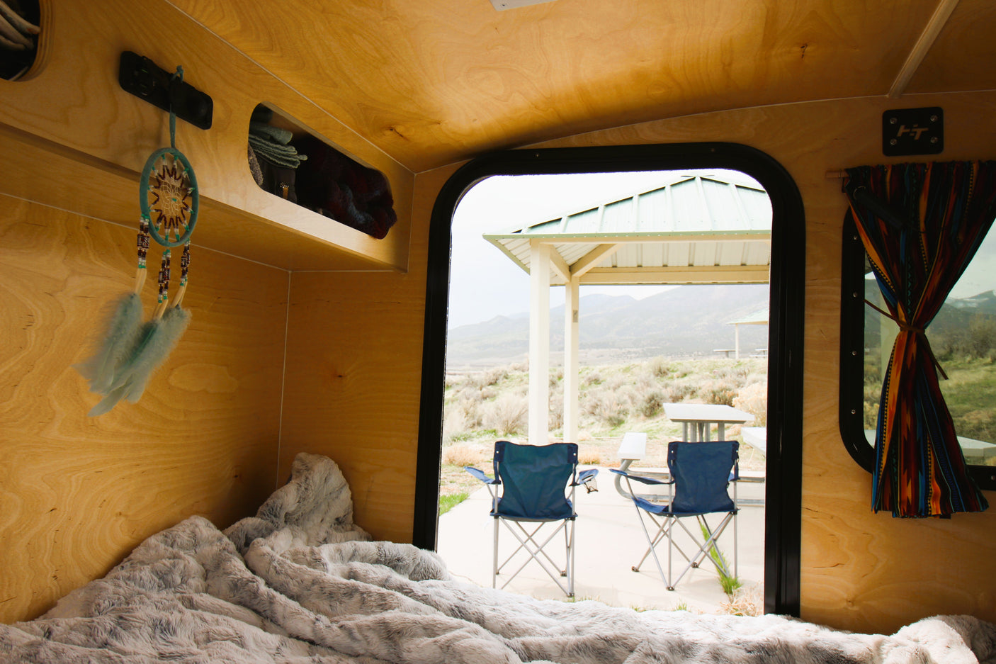 Inside a cozy RV rental: soft bed, dream catcher, and stunning mountain campsite views.