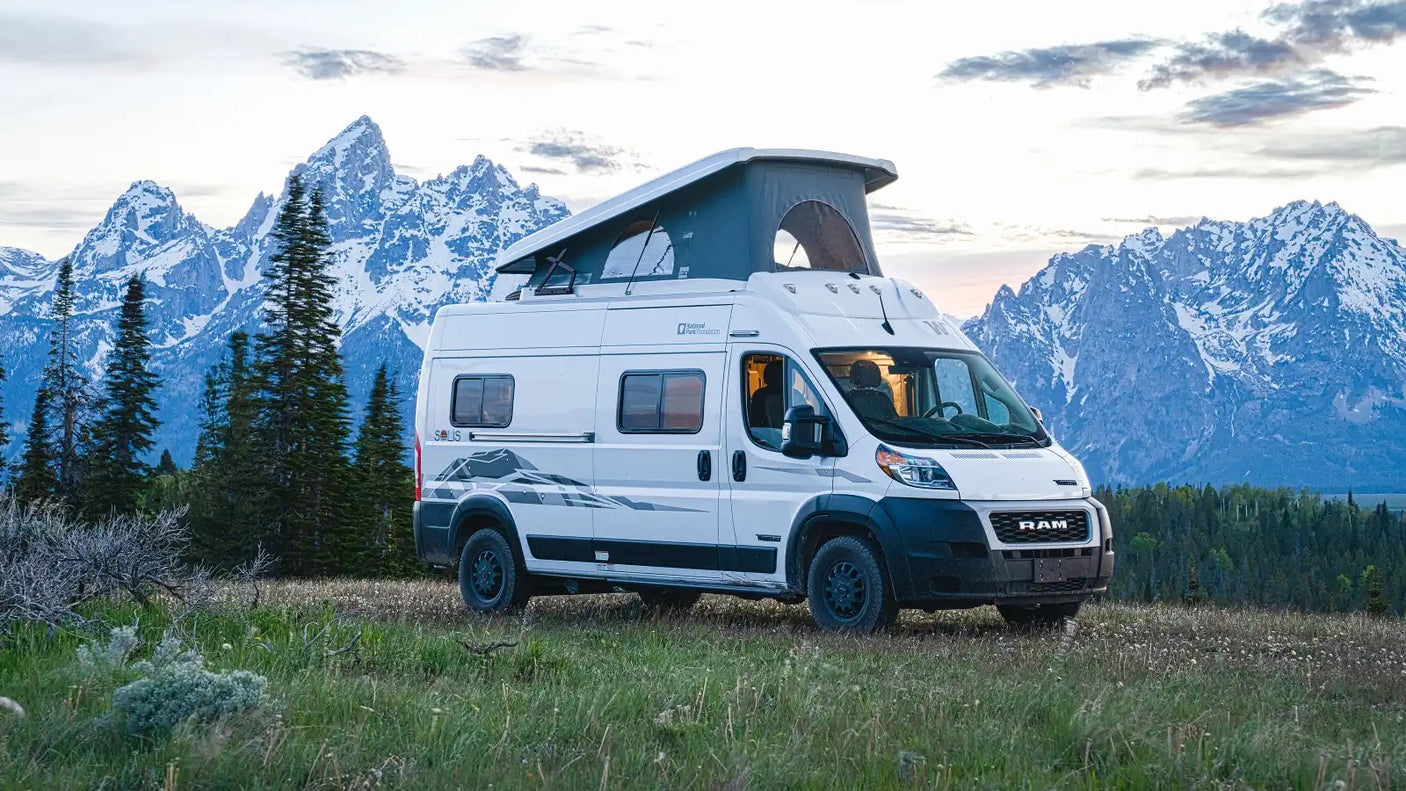 White camper van RV rental with pop-up roof against majestic snow-capped mountains, perfect for an outdoor adventure.
