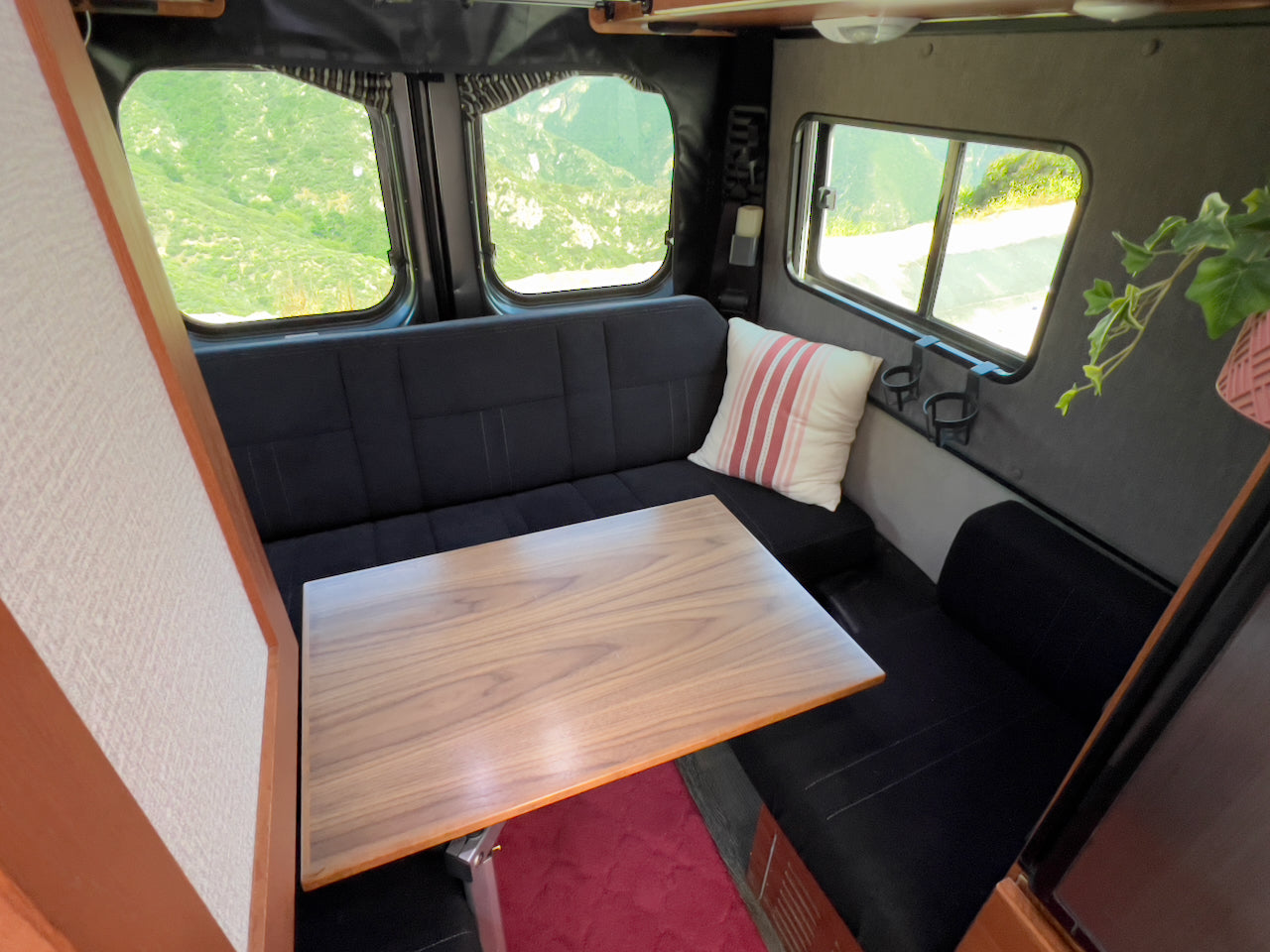 This RV rental interior features a functional dining area with black benches, a wooden table, and beautiful outdoor views.