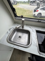 Inside an RV rental, this kitchen features a modern sink, marble-look counter, and covered stovetop, with an outdoor view.